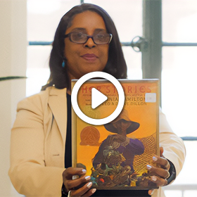 Librarian Jené Brown holding up the book Her Stories: African American Folktales, Fairy Tales and True Tales.