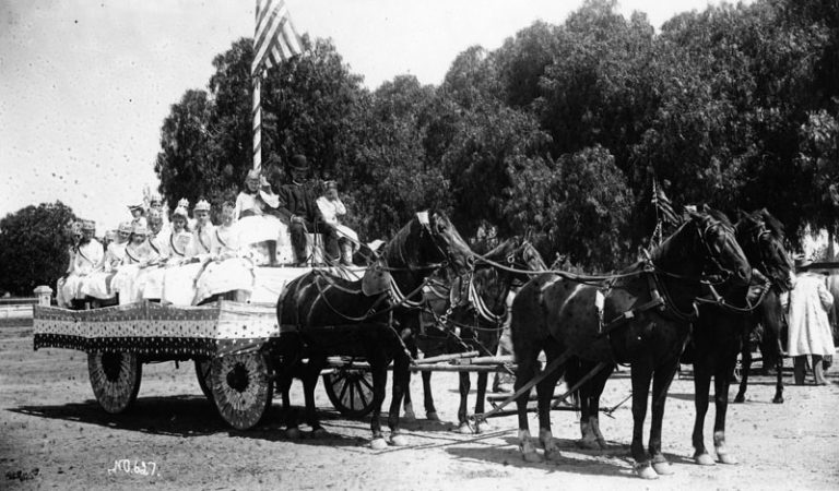 A horse-drawn wagon carries costumed participants in a 4th of July parade in Santa Ana.