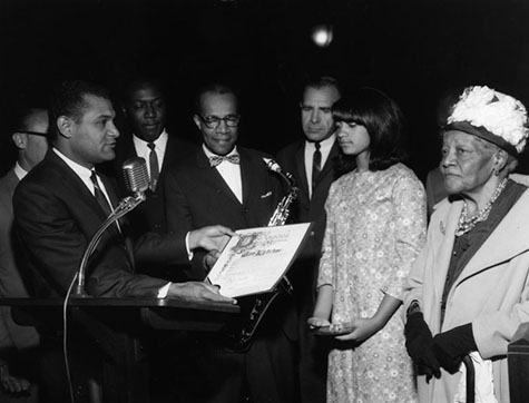 Jazz musician Joe Lutcher is honored with a Los Angeles City Council proclamation, presented by Rosalind Wiener Wyman and, Billy Mills as his family watches. 