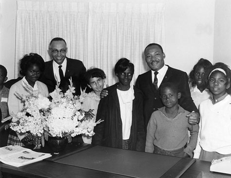 Martin Luther King, Jr. poses for Rolland Curtis at the Second Baptist Church, where King delivered a sermon to a standing-room-only crowd of 2,000 people. Reverend Thomas Kilgore, the pastor of Second Baptist, is standing to the left of King.