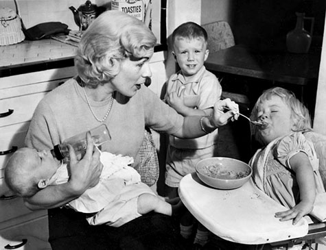 mom feeding baby while brother looks on