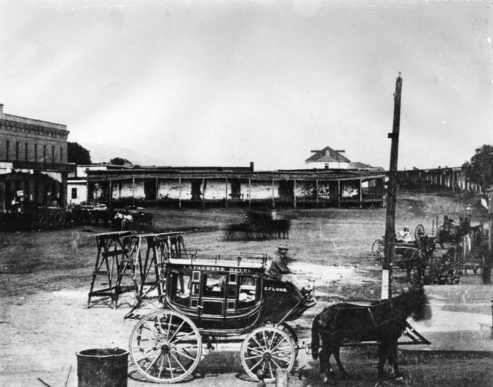 Lafayette Hotel stagecoach near the adobes in Calle de los Negros circa 1870, presently Alameda Street near Union Station and Terminal Annex Building. The old Antonio Coronel adobe is in the background.