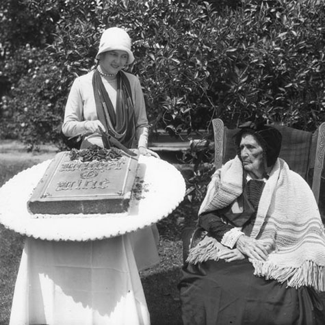 very aged woman is presented a large cake decorated in the shape of a book entitled, "Mother Mine," on Mother's Day in Montebello. 1928