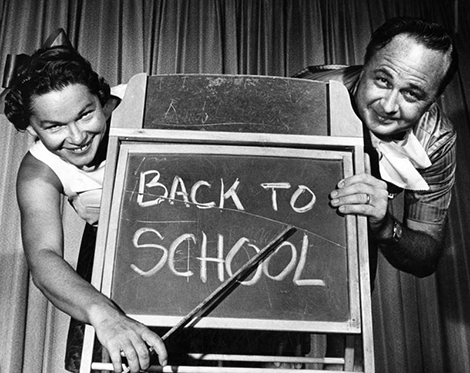 a man and a women point at a back to school sign on a chalk board