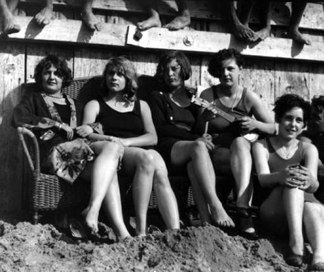 Beach goers in swim suits sit on a wicker sofa and on the sand at the 1928 Pacific Southwest Exposition in Long Beach.
