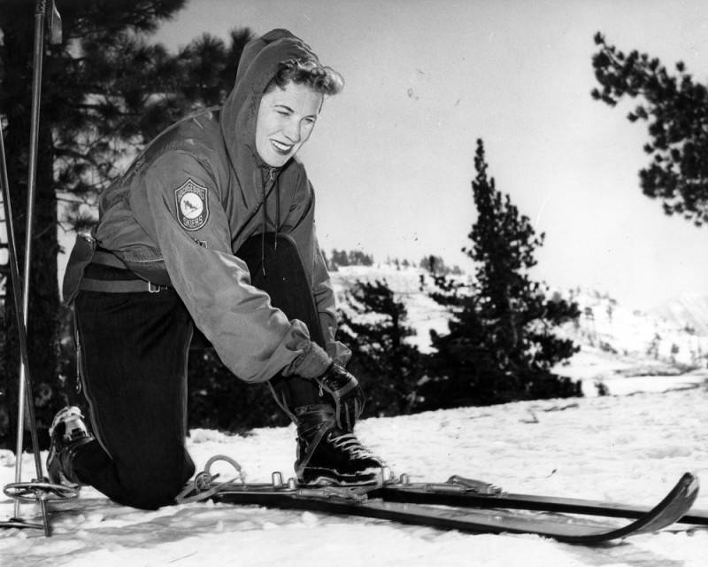 women in the snow bending down to check skis