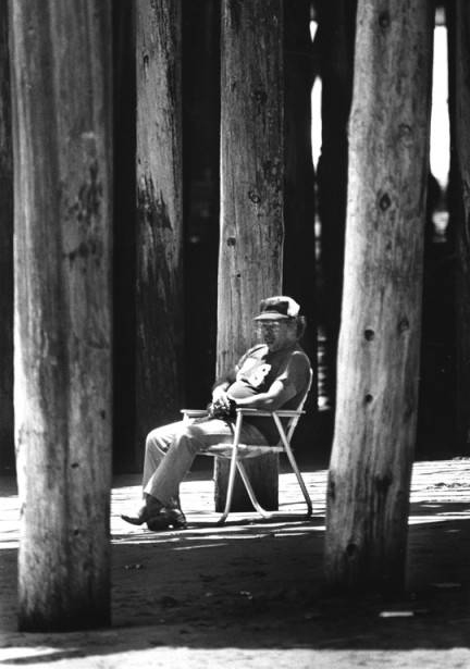 man on lawn chair in between pier pylons