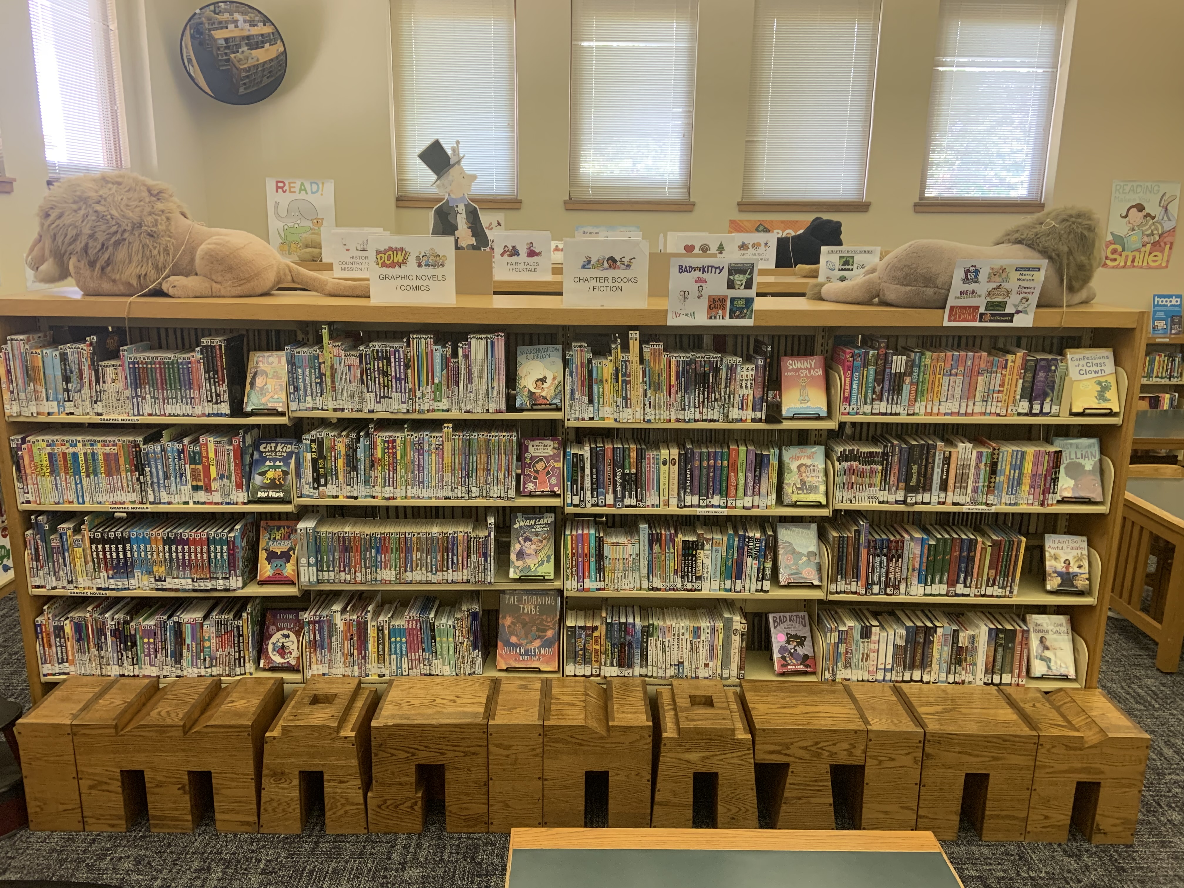 11 oak stools–located in the children’s reading area of the branch in front of a row of bookshelves–spell out the word “IMAGINATION.” 