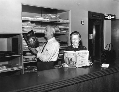 A man and woman consult the Hollywood Branch Library’s popular collection of telephone books, his is from Pittsburgh and hers is from Amsterdam