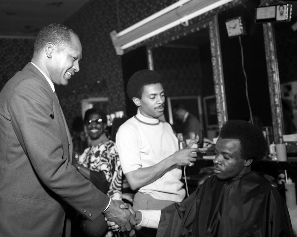 Councilmember Tom Bradley (at left) is shown shaking hands with an unidentified man sitting in a barber's chair