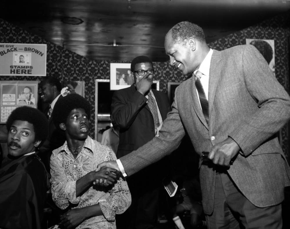 Councilmember Tom Bradley is shown shaking hands with unidentified customers and staff inside the Magnificent Bros Hair Salon 2