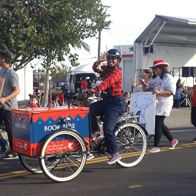 women riding a bookbike and waving