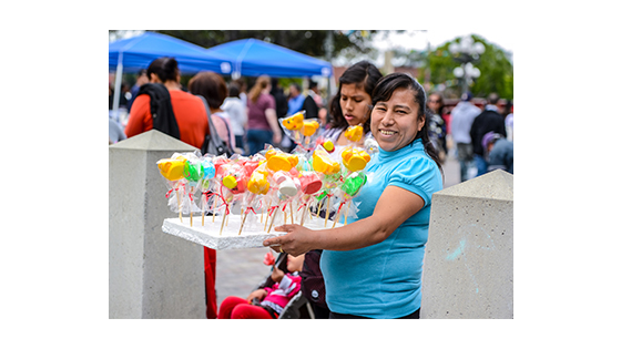 a smiling street vendor holding up the snacks she is selling