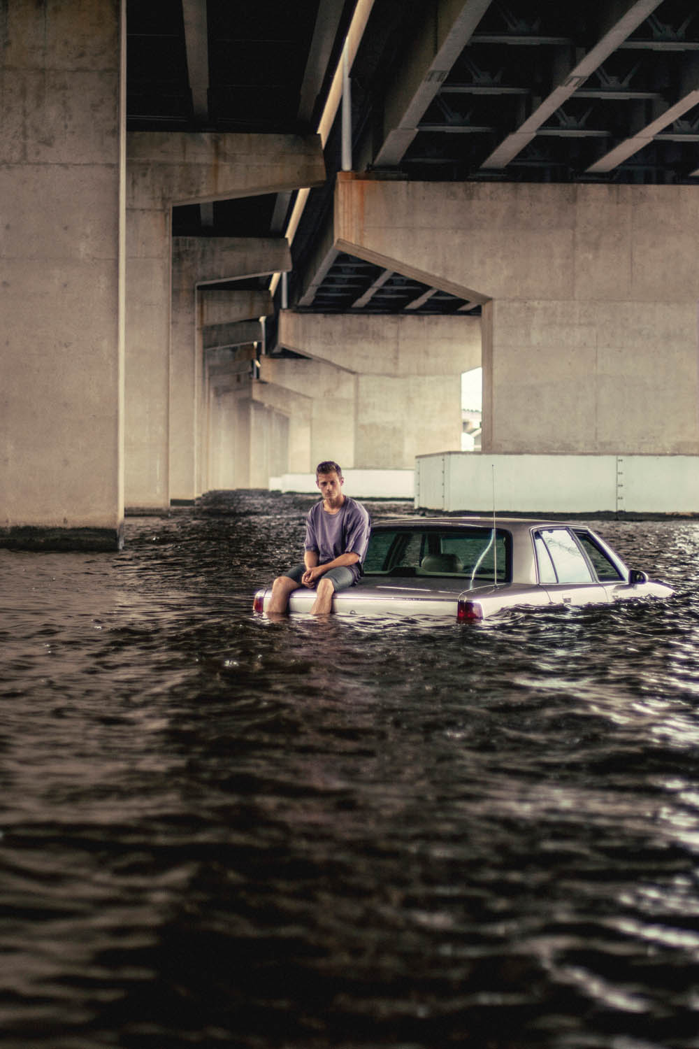 young man sitting on the trunk of a car submerged in a river